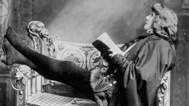 Bernhardt como Hamlet, sentada em um sofá com livro na mão