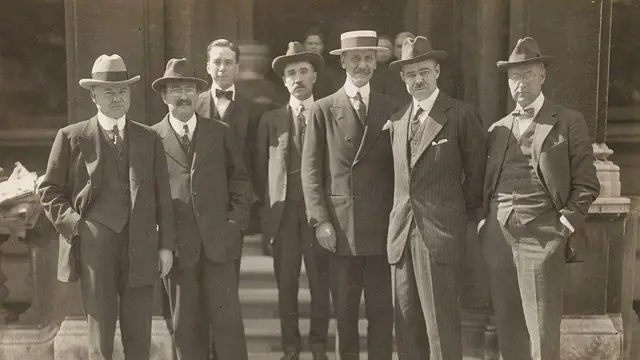 Sete homens com trajes antigos olhando para câmera