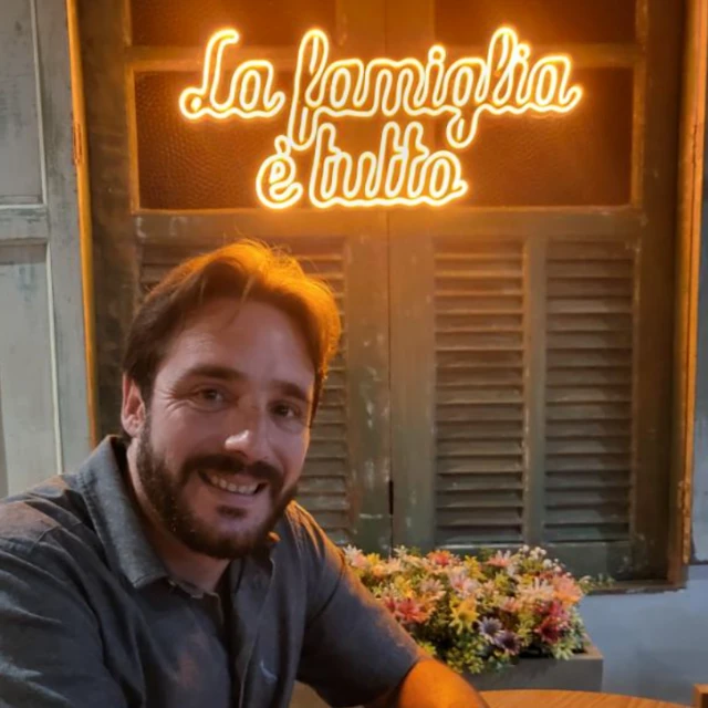 Dono de restaurente italiano sorri em frente de um painel luminoso que diz: La familgia é tutto