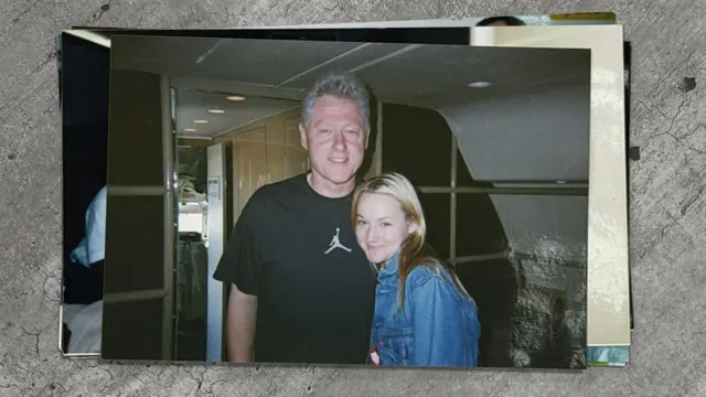 Bill Clinton, an older man with short grey hair, stands close to a young woman, Chauntae Davies. Clinton is in a black short-sleeve t-shirt that has the Air Jordan logo on it. Davies is wearing a light-washed jean jacket. They are inside a plane.