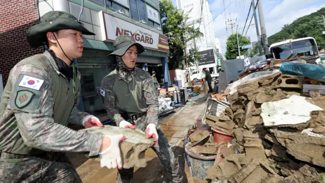 迷彩柄の軍服を着た2人の韓国軍兵士が、道路に落ちた泥だらけのがれきの山から大きな岩片を取り除いている