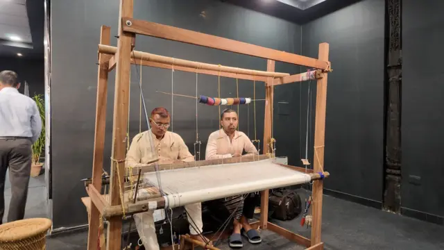 প্রদর্শনীতে হাতেকলমে জামদানি বোনা দেখাচ্ছেন ওস্তাদ ও সাগরেদ তাঁতি
