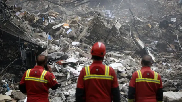 Arama kurtarma ekipleri Amerika ve İsrail'in saldırıları sonucunda Tahran'da yıkılmış bir binanın yanında duruypr