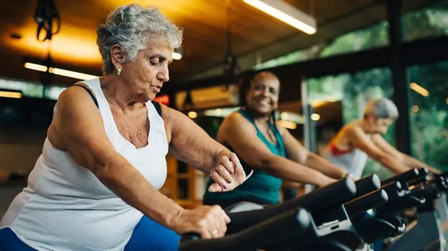 Três mulheres, uma ao lado da outra, fazendo exercício em bicicletas ergométricas