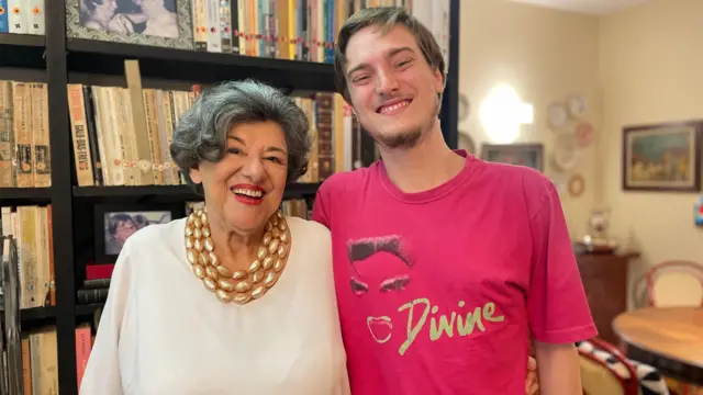 Ruth e Pedro sorrindo, abraçados,onabet b cream 15gmfrente a estanteonabet b cream 15gmlivros