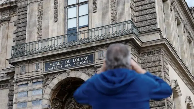 Човек фотографише разбијени прозор заштиц́ен дрвеном плочом у музеју Лувр после пљачке накита, пљачка у лувру, крађа у лувру, опљачкан лувр, опљачкан музеј лувр