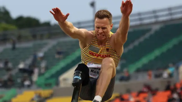 A foto mostra um atleta homem,quantos saques posso fazer na greenbetspele clara, dando um salto. Ele não tem a perna direita e está vestindo uma camiseta regata listradaquantos saques posso fazer na greenbetsamarelo.