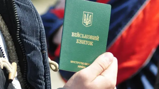 Чоловік тримає у руці військовий квиток 
