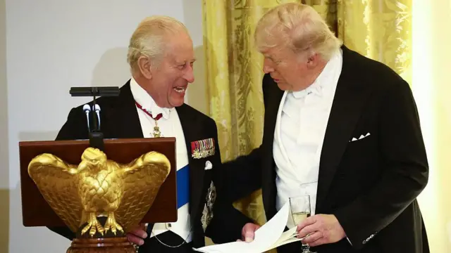 Trump ve İngiltere Kralı şaaşalı bir salondaki devlet Yemeği sırasında sohbet ederken gülümsüyorlar.
