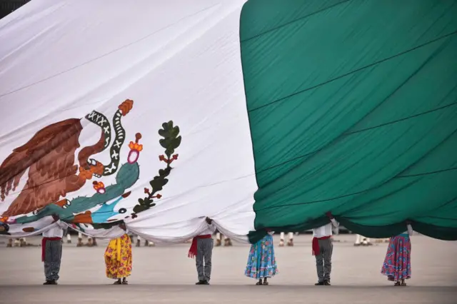 Bandera de México sobre seis personas en una plaza