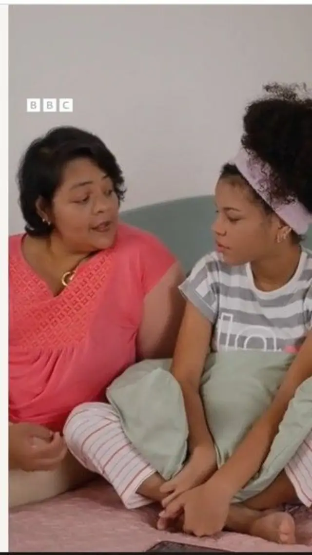 Iya ati ọmọ rẹ obinrin joko sori ilẹ, wọn n wo ara wọn loju