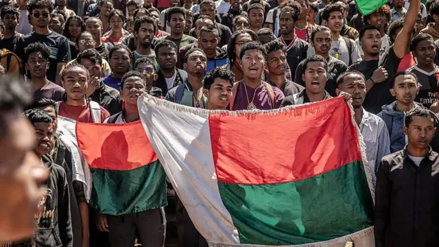 Students dey sing national anthem while dem dey hold Malagasy flags as dem gada to protest.