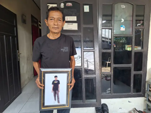 Ayah Bertrand, Yaya membawa foto Bertrand di depan rumahnya