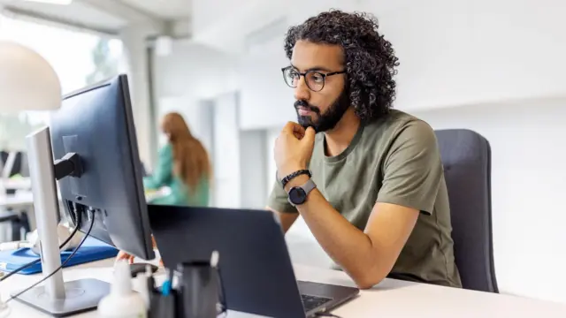 Ọkunrin kan jokoo siwaju ẹrọ kọmputa, o fi ọwọ kan sibi irugbọn rẹ pẹlu awo loju.