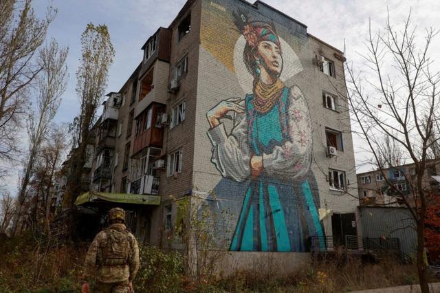 Un soldado ucranino pasaba por un edificio con un mural de una mujer