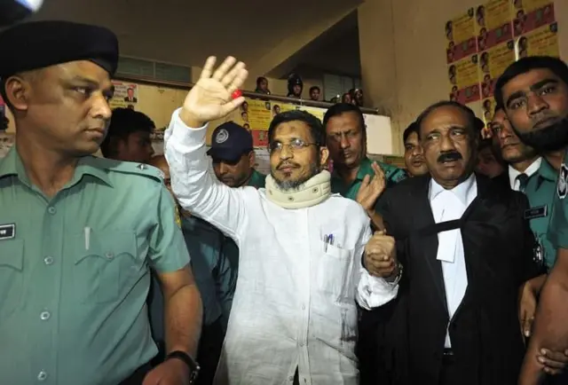 দশট্রাক অস্ত্র মামলায় লুৎফুজ্জামান বাবরকে আদালতে হাজিরা দিতে নেওয়া হয়েছে। হাত নাড়ছেন তিনি। সাথে পুলিশ ও আইনজীবী রয়েছে।