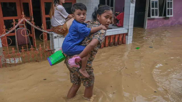 Seorang anak menggendong adiknya menerobos banjir di Kelurahan Kampung Salo, Kendari, Sulawesi Tenggara.