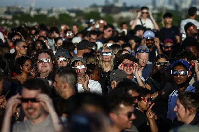 Personas utilizan gafas protectoras especiales mientras observan el eclipse desde Primrose Hill, en Londres.