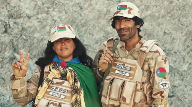 د یاسمه بلوچ او وسیم بلوچ عکس چې د بي‌اېل‌اې په یونیفورم کې ولاړ دي او کامرې ته ګوري. یاسمه د ازادۍ په نښه دوه ګوتې پورته کړې دي.