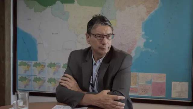 Marcio Pochmann sentado com o mapa do brasil ao fundo