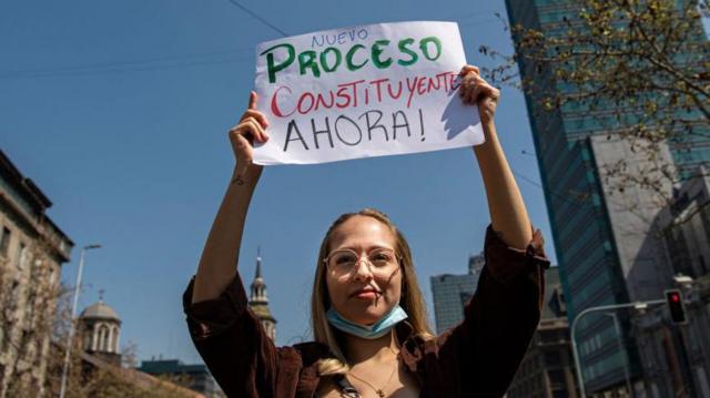 Mulher na rua segura cartaz dizendo: 'Nuevo proceso constituyente ahora!'