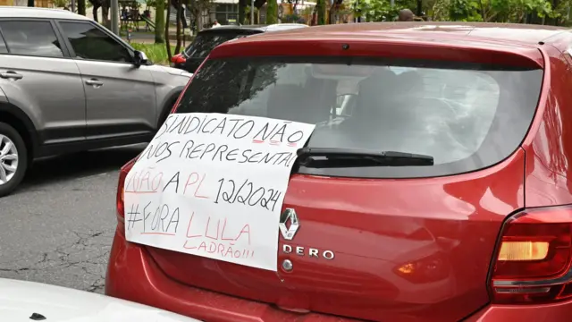 Carro vermelho com um cartaz feito de cartolina colado na traseira, onde se lê "Sindicato não nos representa, não à PLP 12/2024, fora Lula ladrão"