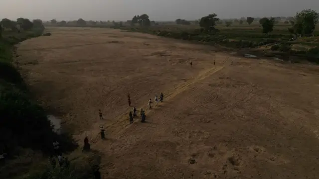 Cette vue aérienne montre des femmes réfugiées traversant les lits asséchés de la Volta blanche pour se rendre dans leurs fermes au Burkina Faso depuis Issakateng-Bausi, à Bawku, dans le nord du Ghana, le 7 décembre 2022.