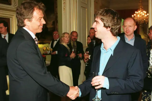 O então primeiro-ministro Tony Blair (à esquerda) apertando a mão de Noel Gallagher.