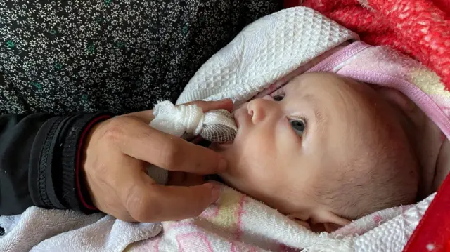 امرأة في غزة تطعم ابنها قطعة تمر بدلاً من الحليب في ظل انقطاعه