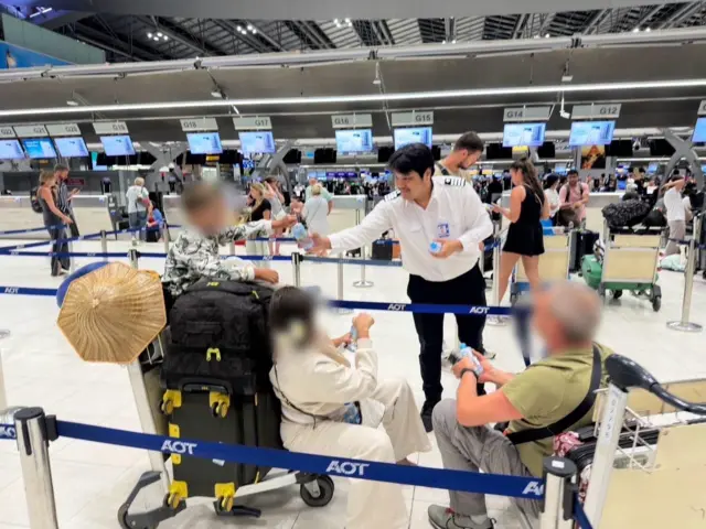 သုဝဏ္ဏဘူမိလေဆိပ်မှာ သောင်တင်နေတဲ့ ခရီးသည်တချို့ကို ရေသန့်ဝေနေတဲ့ လေဆိပ်ဝန်ထမ်းတစ်ဦး 