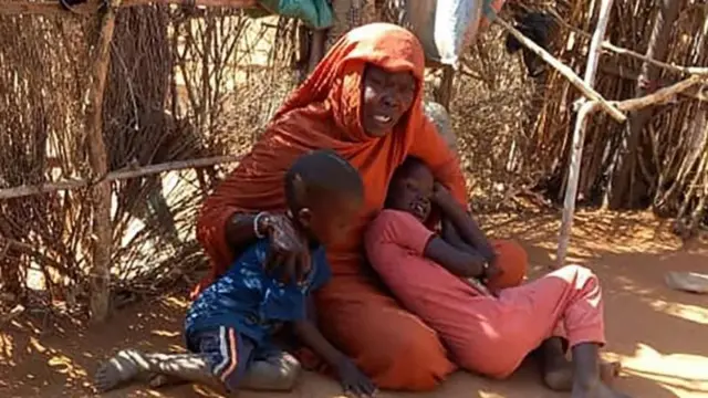 መሬት ላይ ቁጭ ብላ ሁለት ልጆቿን ያቀፈች እናት