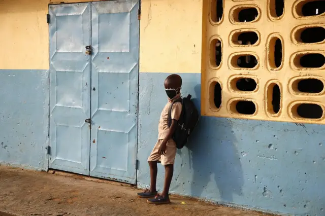 Un élève portant un masque facial se tient à l'extérieur d'une classe.
