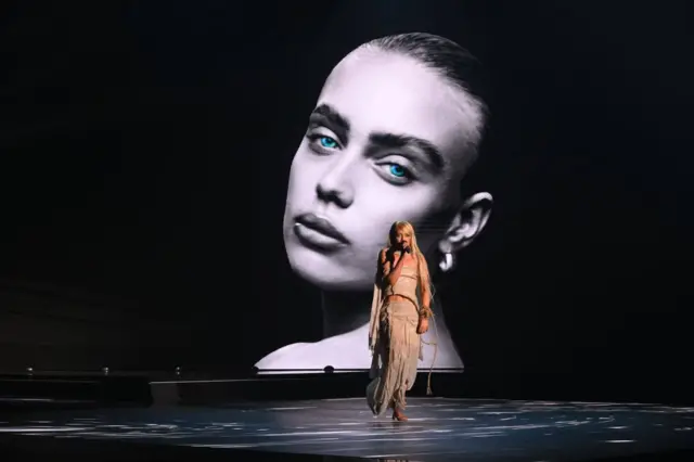 Певачица у беж хаљини с ресама, дуге плаве косе