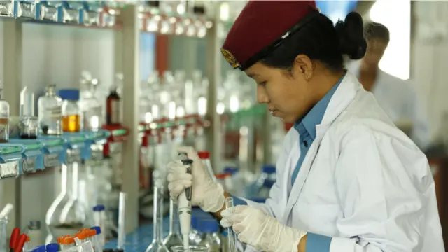 नेपाल प्रहरीको प्रयोगशालामा काम गर्दै एक कर्मचारी, उनले प्रहरीको पोसाक र त्यसमाथि सेतो एप्रोन लगाएकी छन् 