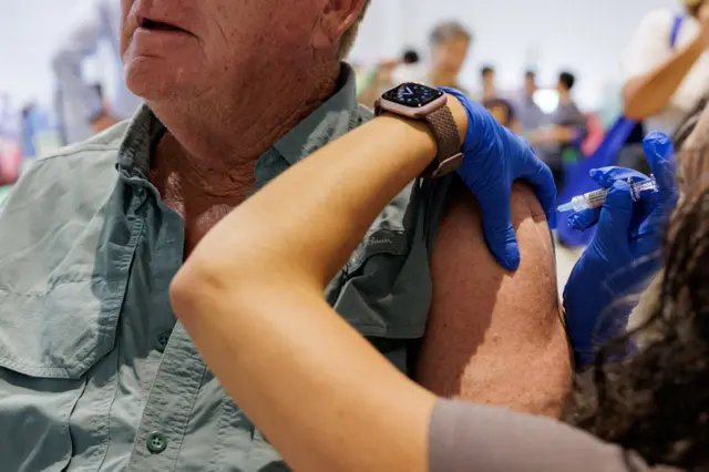 Muškarac sedi dok mu žena daje vakcinu u ruku