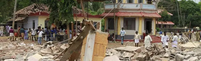 People stand next to debris after a broke out at a temple in Kollam in the southern state of Kerala, India