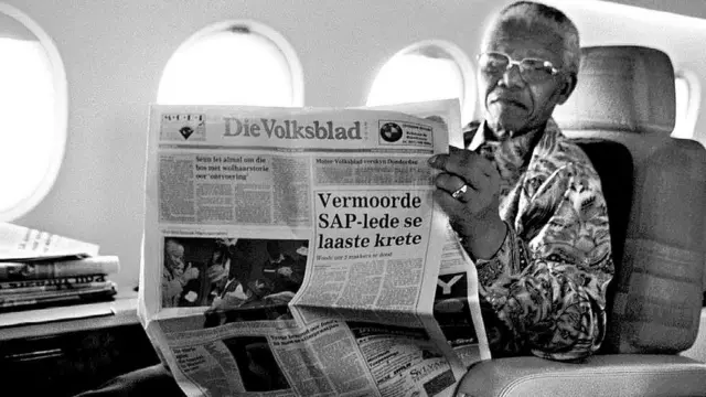 Le président sud-africain Nelson Mandela se détend à bord de l'avion présidentiel avec un exemplaire de Die Volksblad, un journal afrikaans.