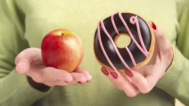 Una mujer sostiene una manzana en una mano y una dona en la otra.