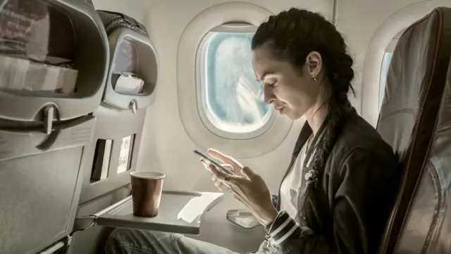 Una persona en un avión, mirando su teléfono