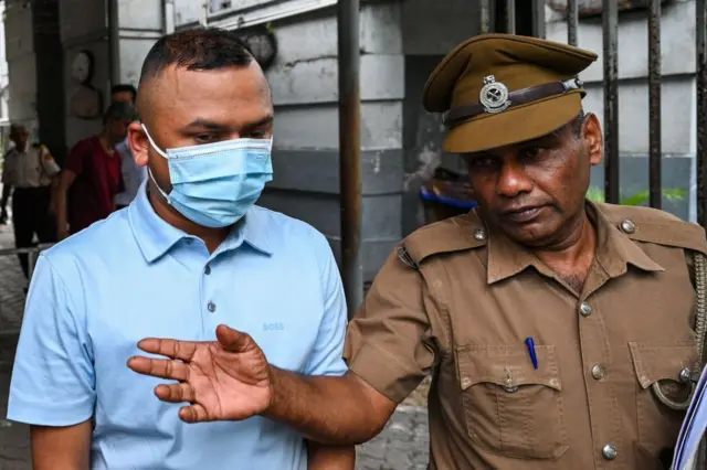 আকাশী রংয়ের পোলোশার্ট ও মুখে মাস্ক পরা তামিম রহমানের পাশে হাত তুলে কিছু বলছেন পুলিশের একজন সদস্য। 