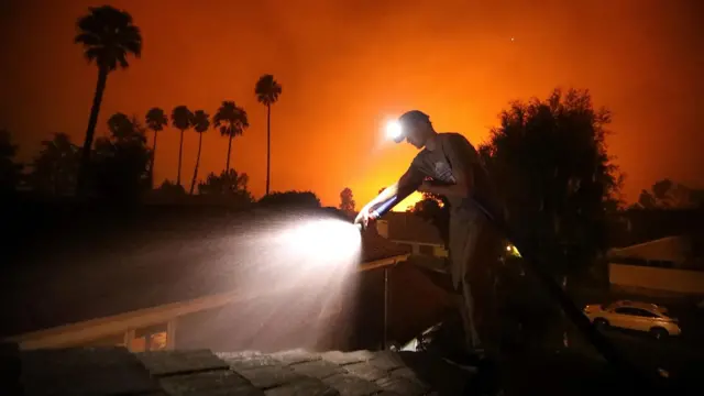 Pessoa com uma mangueira tentando controlar os incêndios na Califórnia