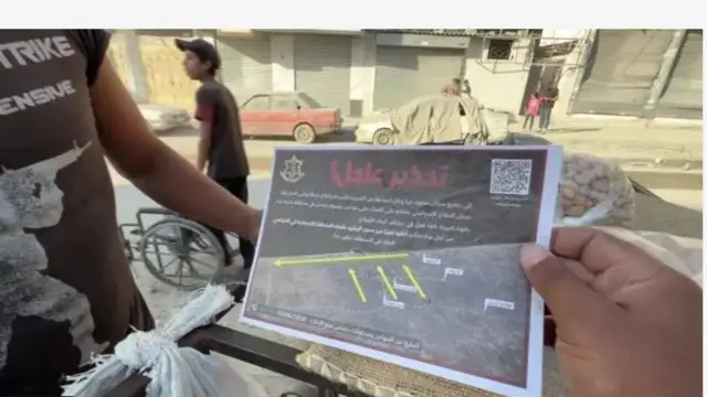 Aworan yii ṣafihan ọwọ to mu iwe ikilọ pe ki wọm kuro niGaza dani, ede Larubawa ni wọn fi kọ ọ. Ẹnikan ti oju rẹ ko han wa niwaju ọwọ to mu iwe naa dani, bẹẹ ni ọmọkunrin kan to n ti kẹkẹ han nibẹ pẹlu