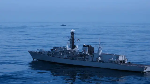 Военный корабль в море, на заднем плане подводная лодка