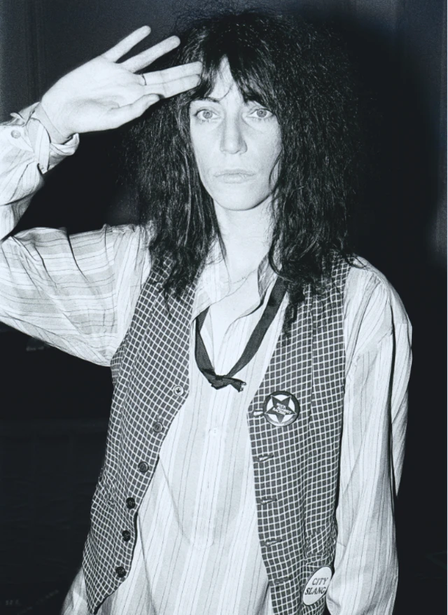 Picha nyeusi na nyeupe ya Patti Smith akiangalia kamera akiwa ameekelea mkono wake juu ya kichwa chake