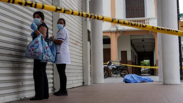 Deux femmes debout à côté d'un magasin fermé à Guayaquil et un cadavre couvert gisant sur le trottoir en arrière-plan