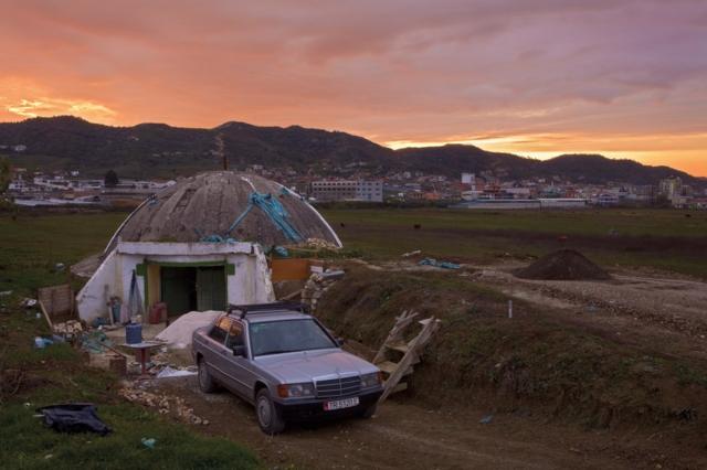 Bunker in Albania with a car next to it and buildings in the background