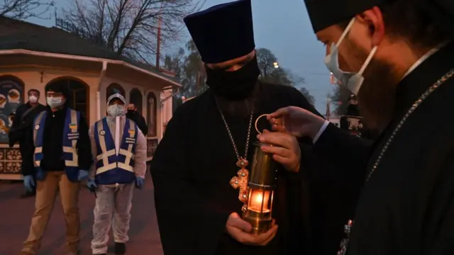 Ukrainian Orthodox priests wearing masks hold a candle with the Holy Fire brought from Jerusalem next to Kiev-Pechersk Lavra monastery in Kiev on April 18, 2020 on the eve of the Orthodox Easter. -