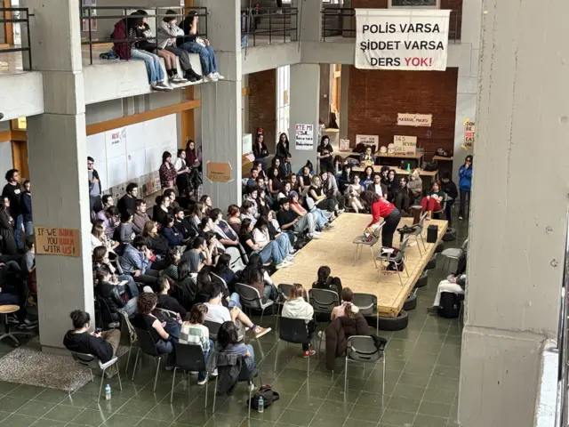 ODTÜ'de bir grup öğrenci etkinlikte görülüyor. Duvarda "polis varsa, şiddet varsa ders yok" yazılı pankart asılı