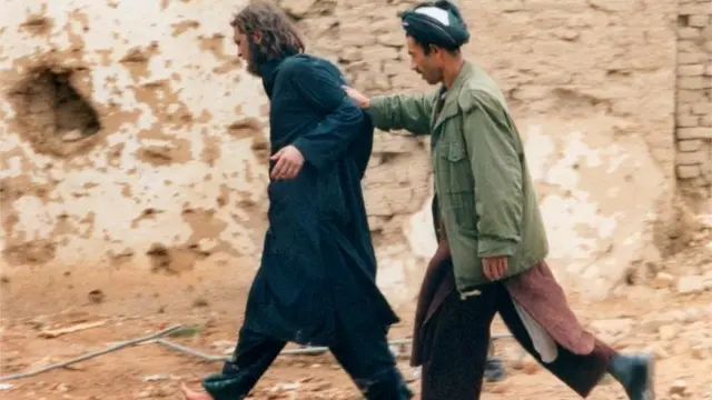 جان والکر لینډ (کیڼ) په افغانستان کې د شمالي ټلوالې د یوه وسله وال له خوا تر نیول کېدو وروسته زندان ته بېول کېږي - ۲۰۰۱