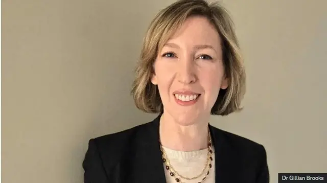 Dr seidman aragaragara aseka mu ifoto ,imisatis ye yayisokoje imanuka,yambaye ikote ry'umukara.